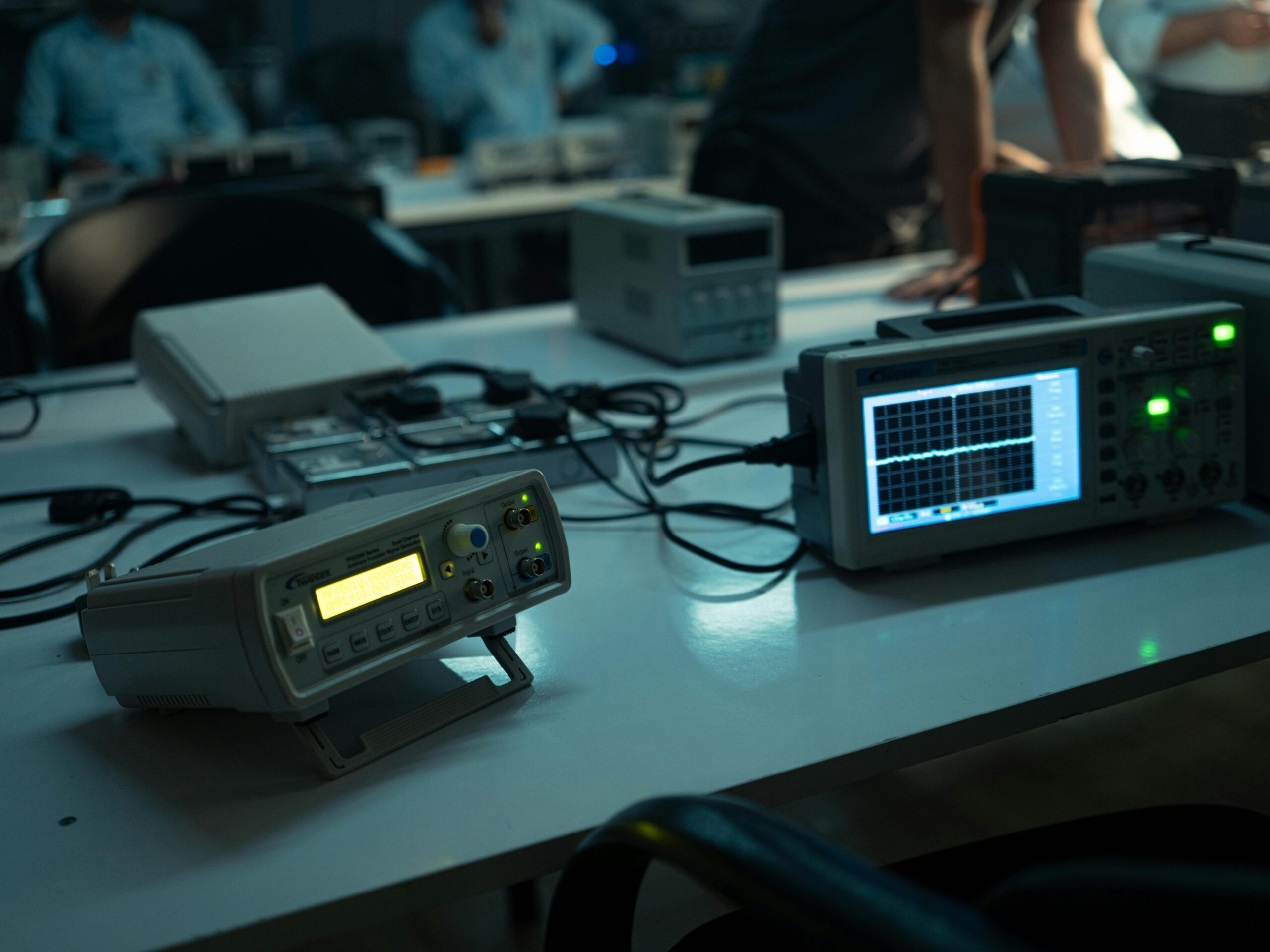 A dimly lit electronics lab featuring oscilloscopes and equipment on desks, creating a technical atmosphere.